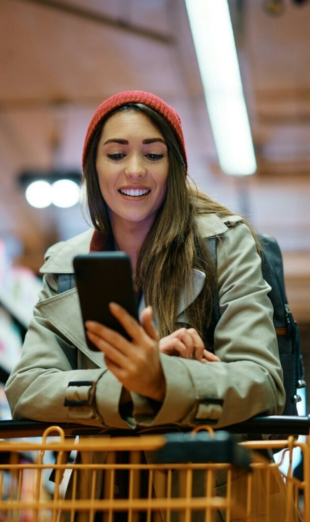 Happy woman using mobile app on her phone while shopping in supermarket.